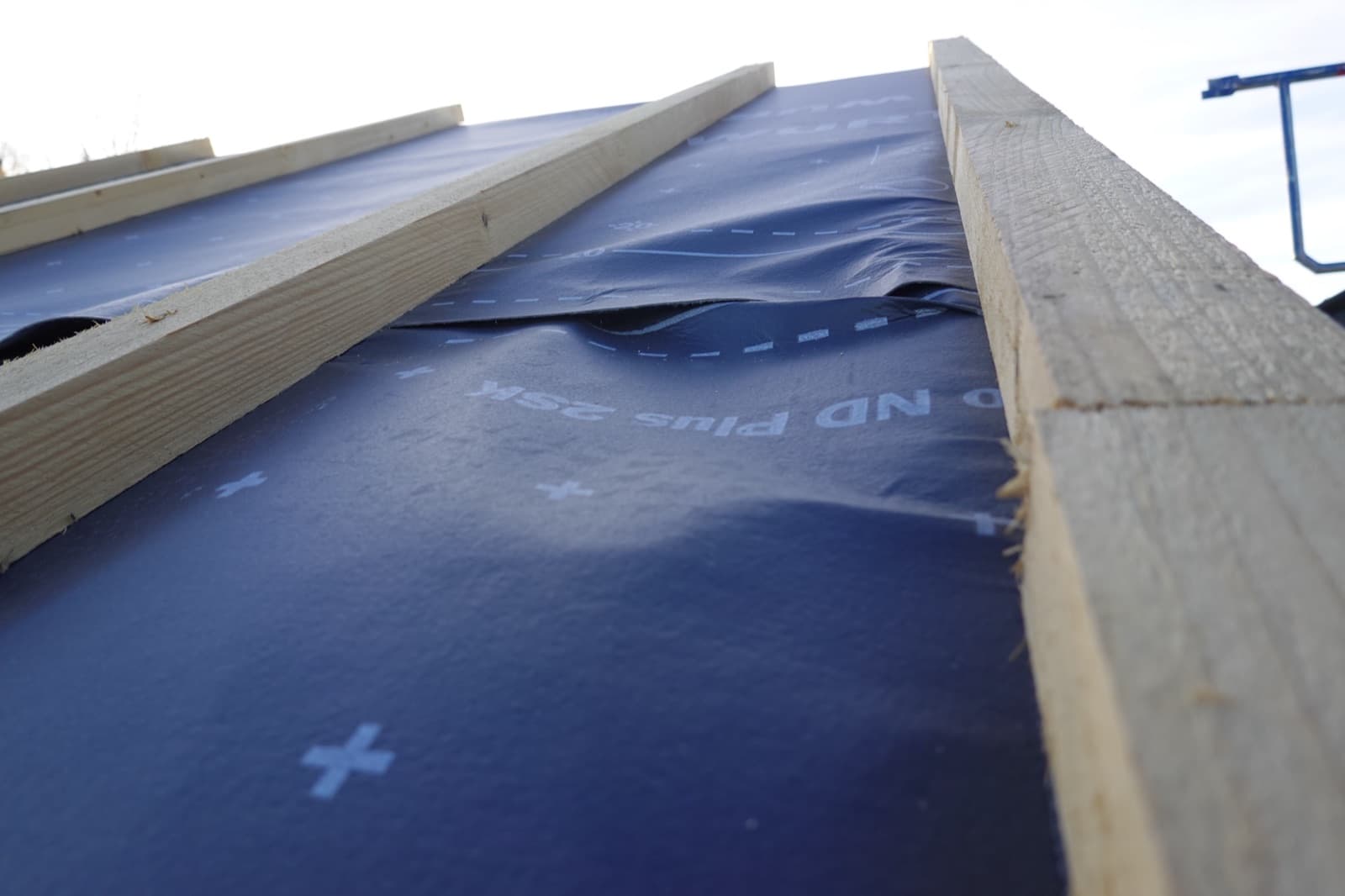 Dachaufbau mit blauer Unterspannbahn, Lattung und angrenzenden Platten