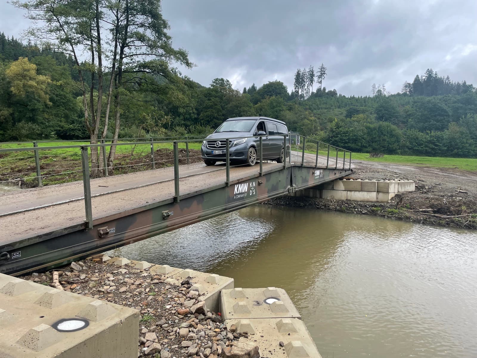 Fahrzeug auf einer militärischen Behelfsbrücke über einen Bach, daneben ausgespülte Ufer