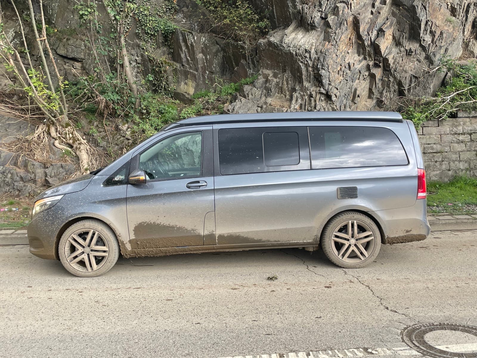 Schlammverkrusteter Kleinbus am Straßenrand unterhalb einer Felswand