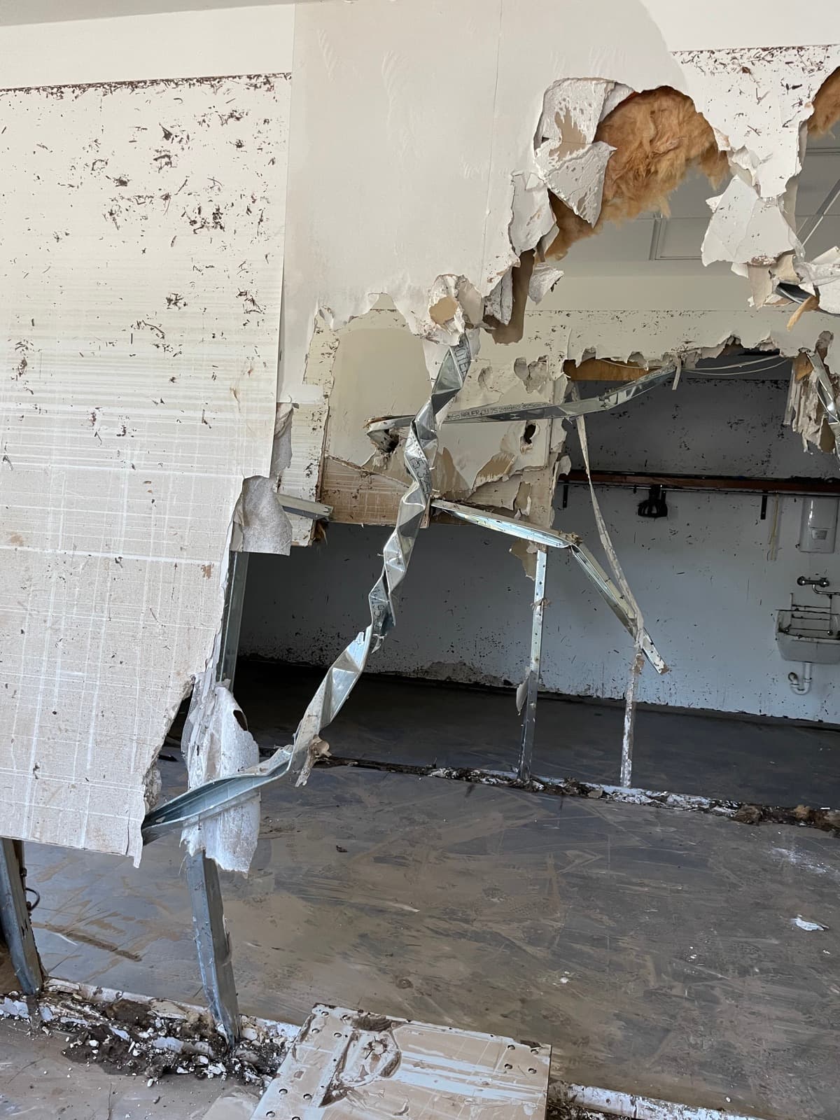 Aufgerissene Trockenbauwand: Gipskartonplatten abgelöst, Ständerprofile verbogen, Dämmung liegt frei