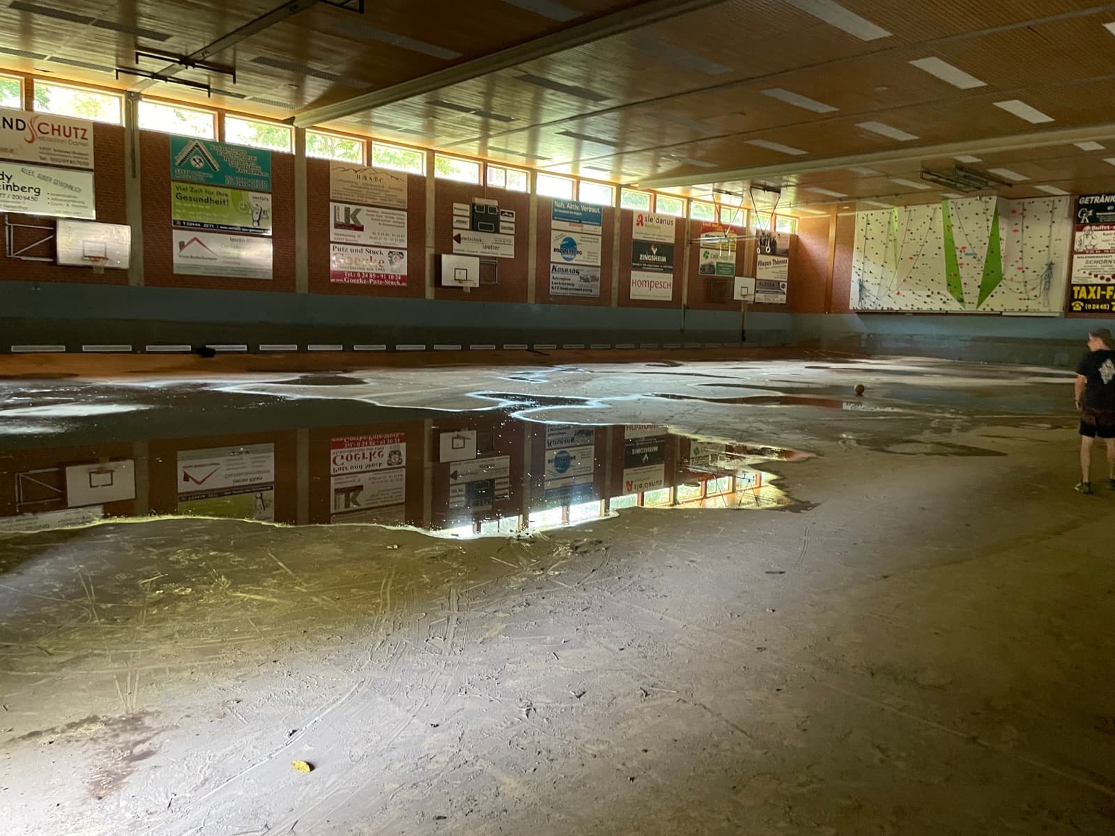 Leergeräumte Sporthalle mit aufgequollenem Hallenboden, stehenden Wasserpfützen und Schlammresten