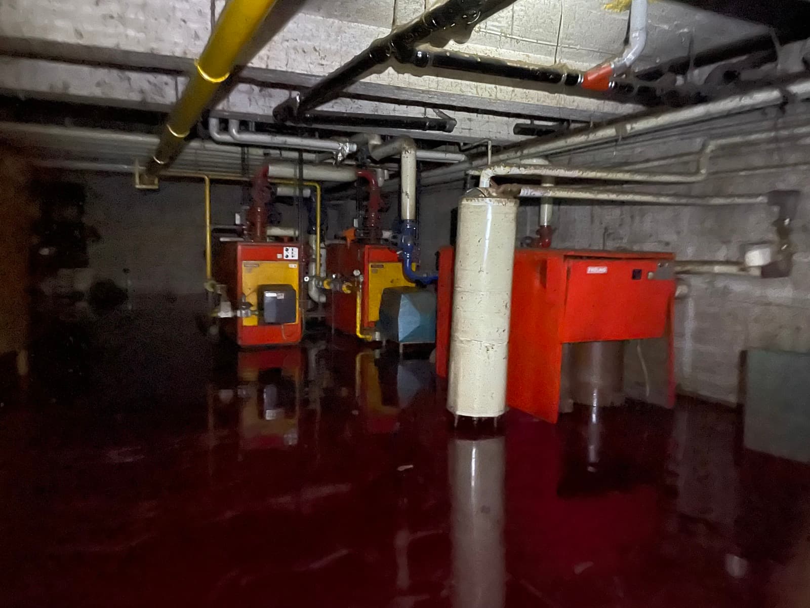 Überfluteter Heizungsraum: Kessel, Brenner und Leitungen stehen in rötlich verfärbtem Wasser