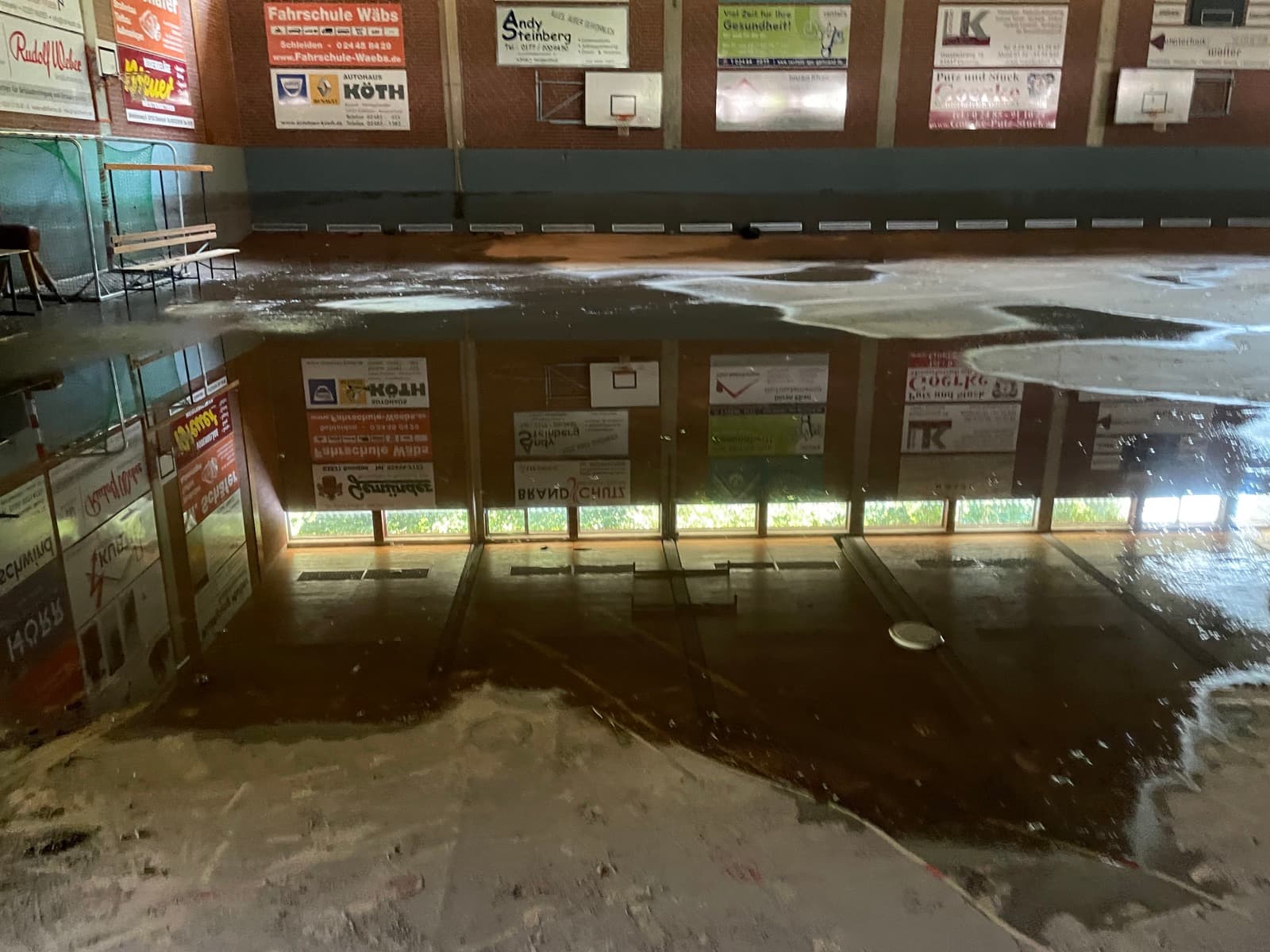 Wasserfläche in einer Sporthalle, in der sich Fenster und Werbetafeln der Hallenwand spiegeln