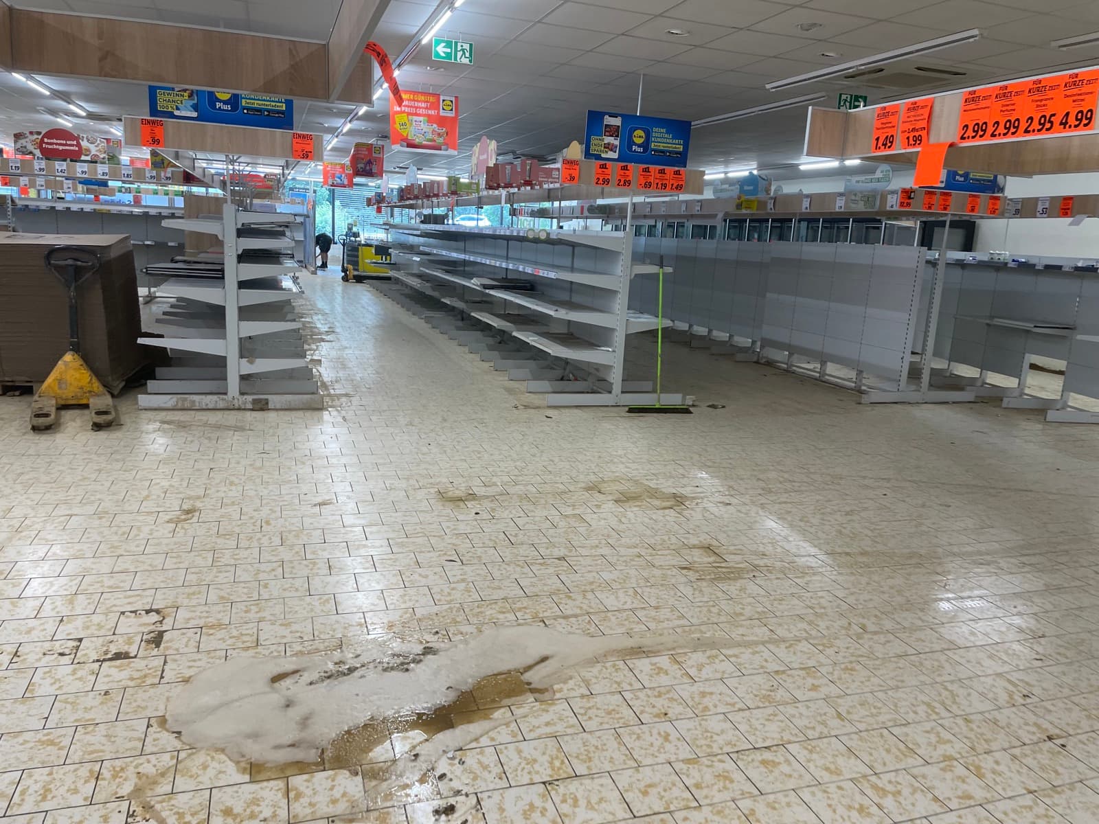 Verkaufsraum eines Supermarkts mit leergeräumten Regalen und Schlammresten auf dem Fliesenboden