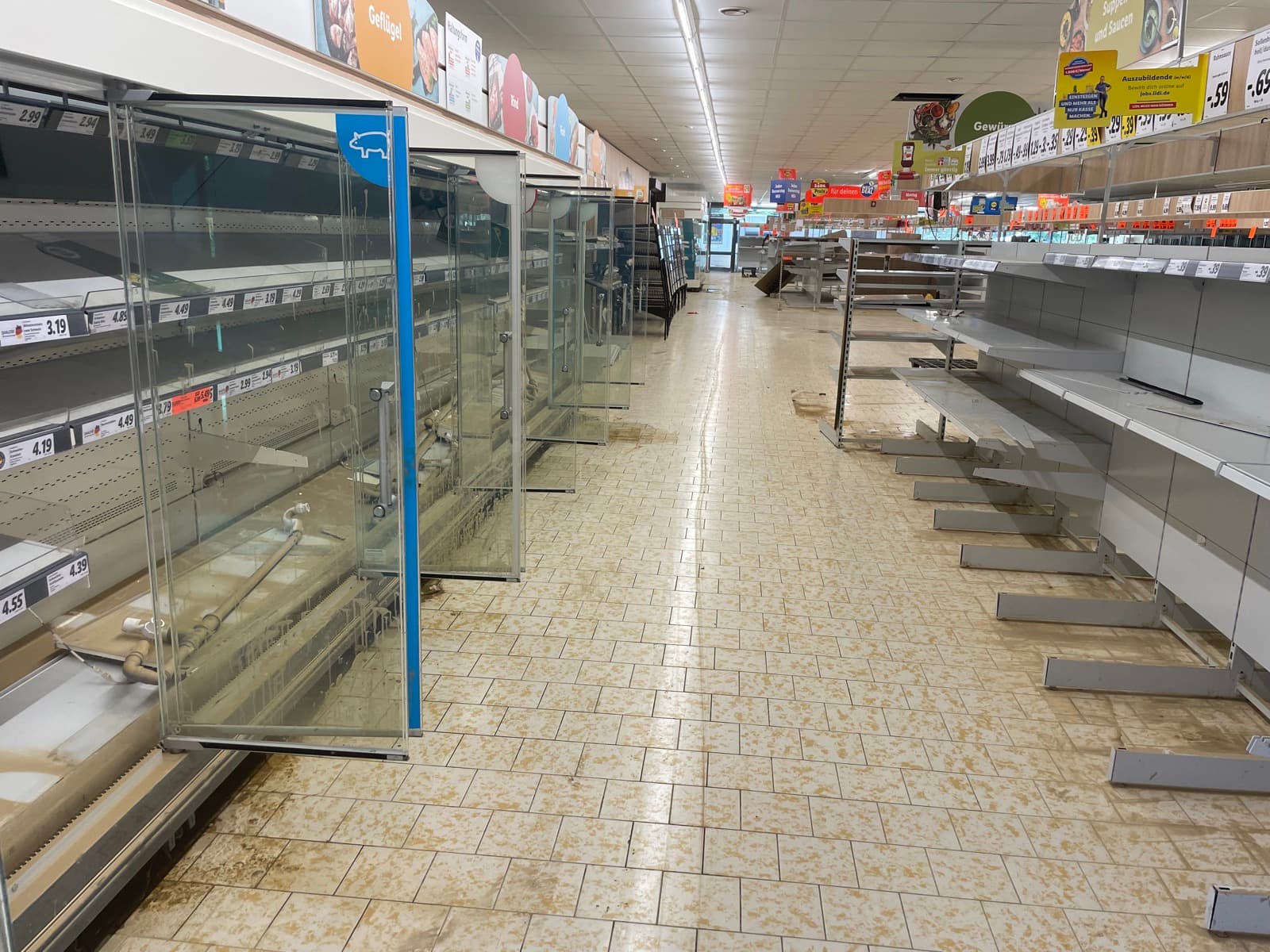 Leergeräumte Kühlregale und schlammverschmierter Fliesenboden in einem überfluteten Supermarkt