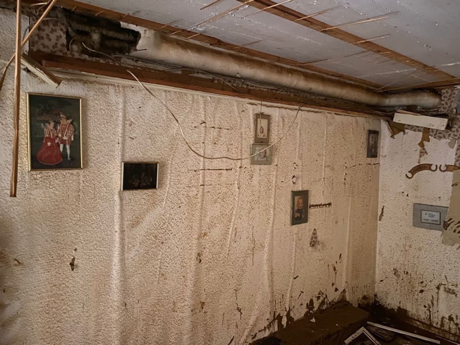Wand eines geräumten Wohnraums mit hoher Wasserlinie dicht unter der Decke, aufgeweichter Putz und noch hängende Bilderrahmen