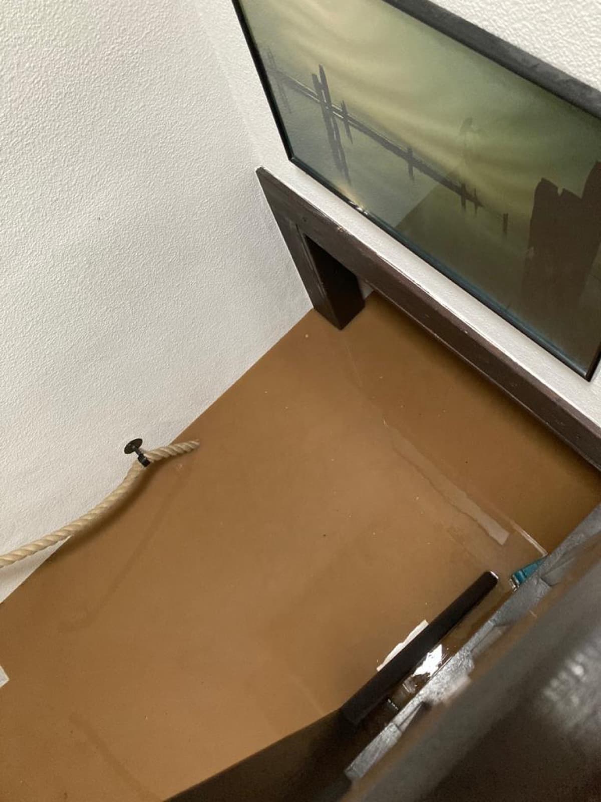 Trübes Hochwasser steht in einem Treppenhaus bis dicht unter ein Wandbild, der Seilhandlauf verschwindet im Wasser