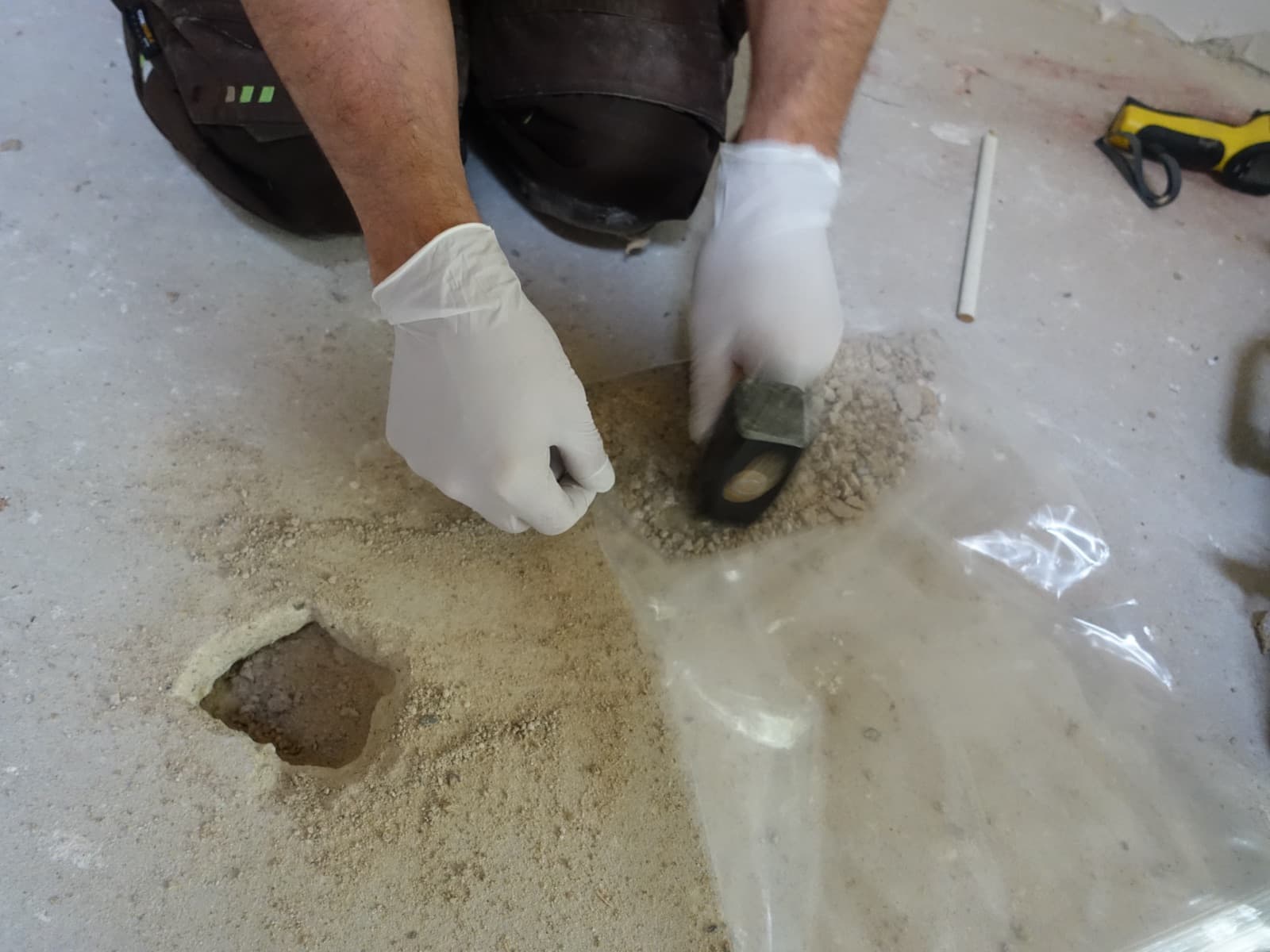 Entnahme einer Materialprobe aus einer Bodenbeschichtung mit Handschuhen und Spachtel